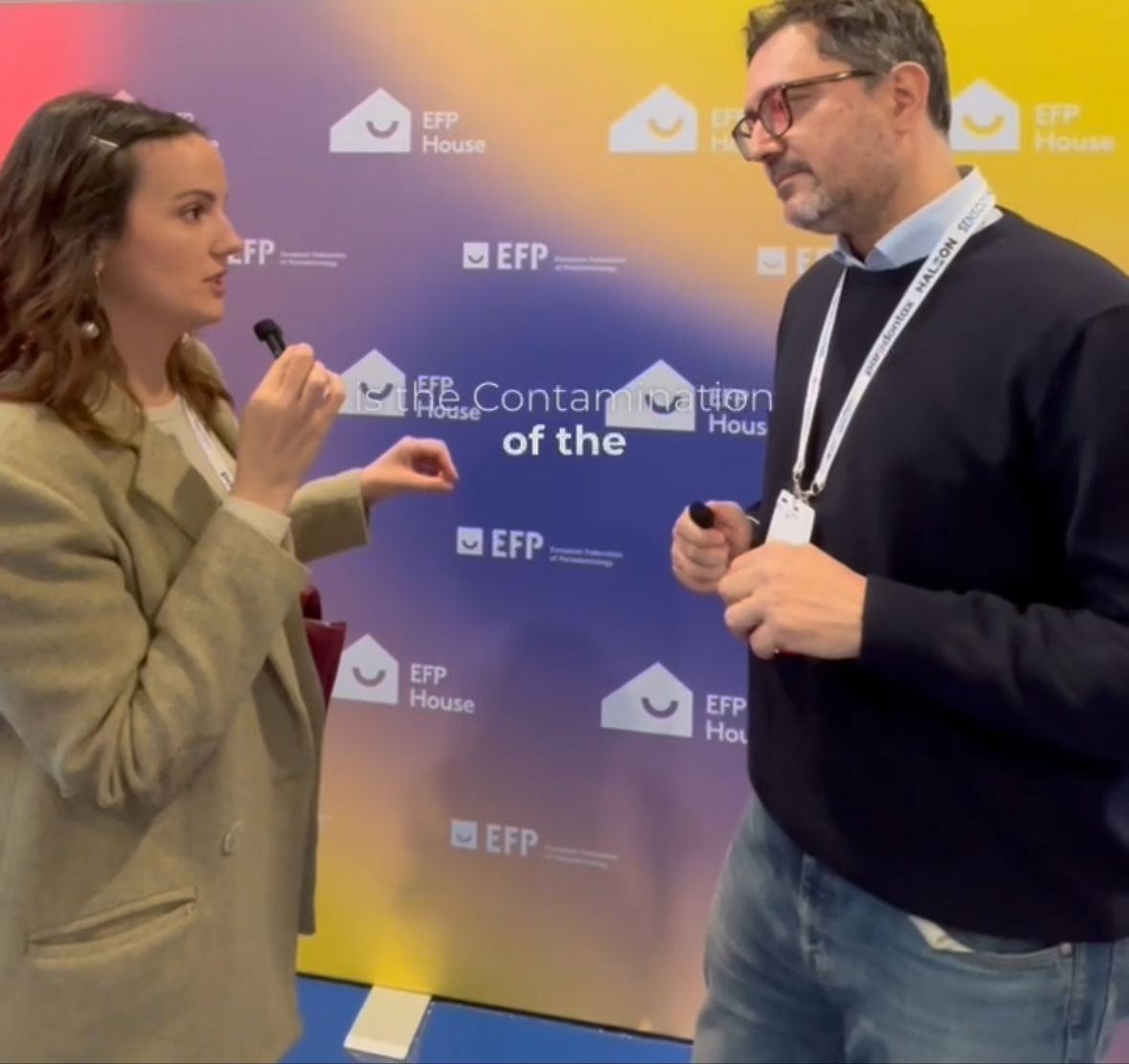 Two people holding microphones in front of a colorful EFP House backdrop during an interview or discussion.