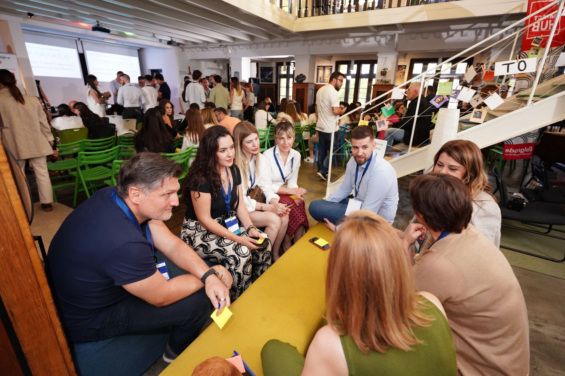 Group of people having a discussion in a modern indoor space with green chairs and large windows.